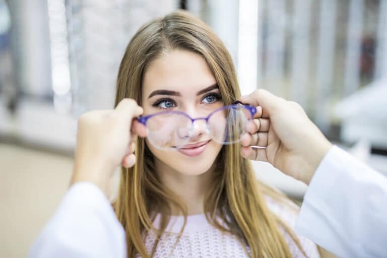 Femme essayant une paire de lunettes bleues, souriant.