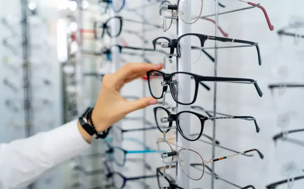 Main choisissant une paire de lunettes noires sur un présentoir dans un magasin d'optique.